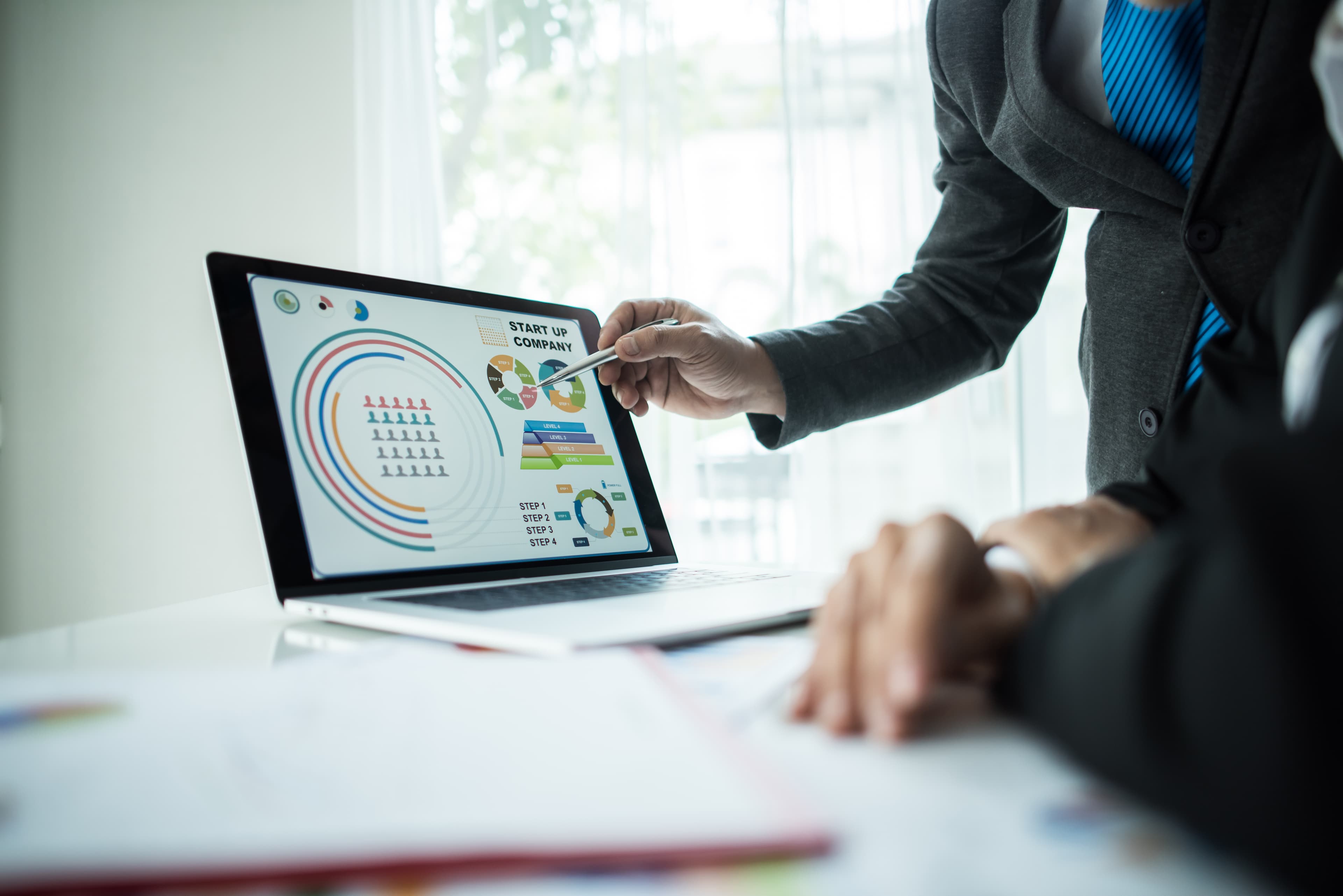 Eine Person im Anzug zeigt mit einem Stift auf Geschäftsdiagramme auf einem Laptop-Display.